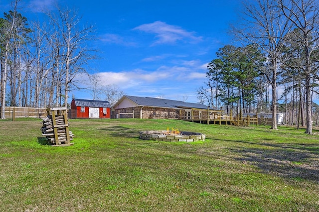 view of yard with a deck, an outdoor structure, a fire pit, and fence