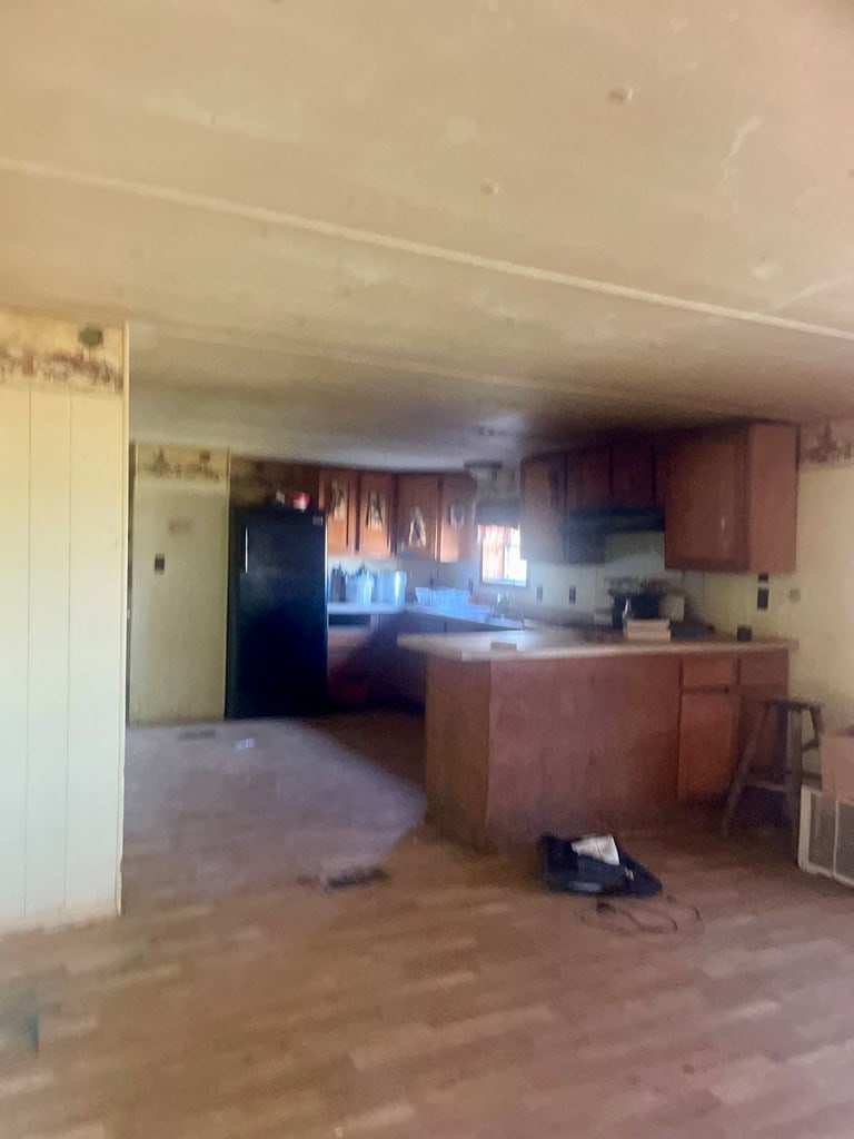 kitchen with brown cabinetry, wood finished floors, and freestanding refrigerator