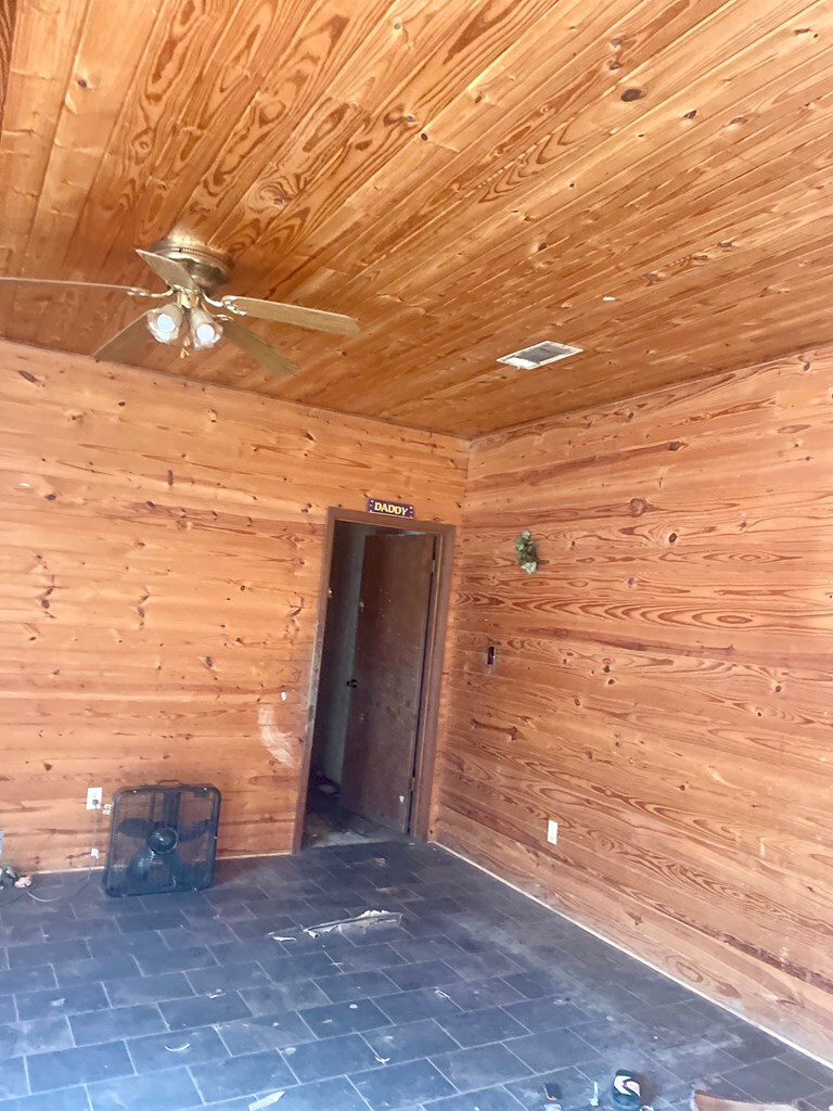 tiled empty room featuring wooden walls, wood ceiling, and a ceiling fan