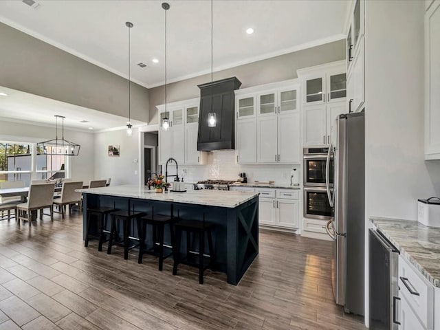 kitchen with a kitchen island with sink, stainless steel appliances, light stone countertops, white cabinets, and decorative light fixtures