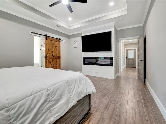 bedroom featuring ceiling fan, a tray ceiling, a barn door, and light hardwood / wood-style floors