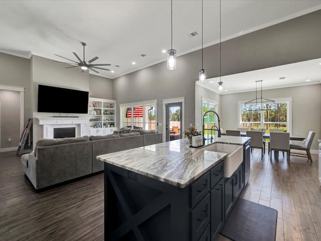 kitchen featuring pendant lighting, sink, ornamental molding, light stone countertops, and an island with sink