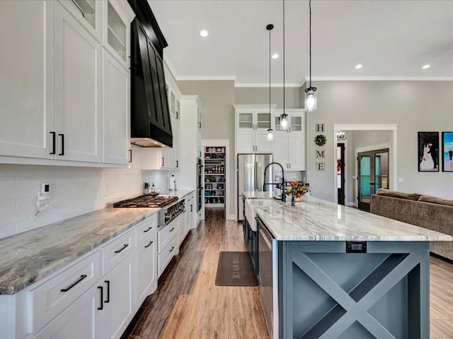 kitchen with hanging light fixtures, a large island with sink, ornamental molding, stainless steel appliances, and white cabinets