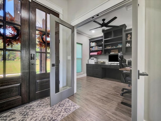 home office with built in desk, wood-type flooring, ornamental molding, ceiling fan, and french doors