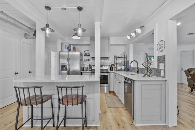 kitchen featuring kitchen peninsula, appliances with stainless steel finishes, light wood-type flooring, sink, and hanging light fixtures