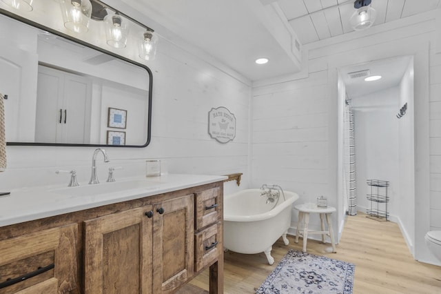 bathroom with a bathing tub, wood walls, wood-type flooring, toilet, and vanity