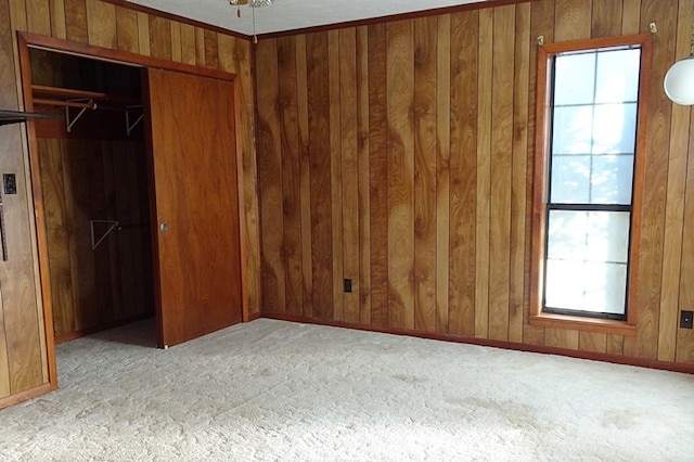 unfurnished bedroom featuring wood walls, ornamental molding, multiple windows, and a closet