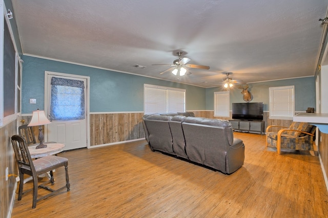 living room featuring a wainscoted wall, wood finished floors, ceiling fan, and crown molding