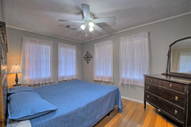 bedroom with wood finished floors, visible vents, ceiling fan, crown molding, and multiple windows