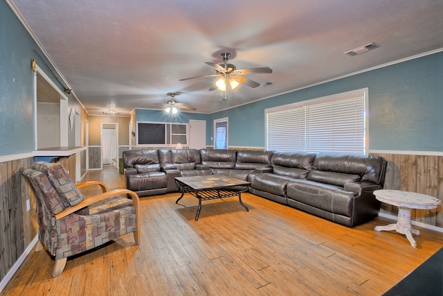 living area with a wainscoted wall, ornamental molding, visible vents, and wood-type flooring
