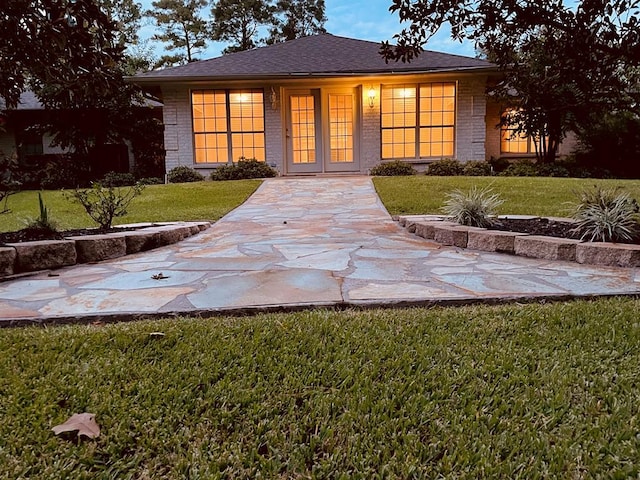 view of front of home featuring a shingled roof, french doors, brick siding, and a front lawn