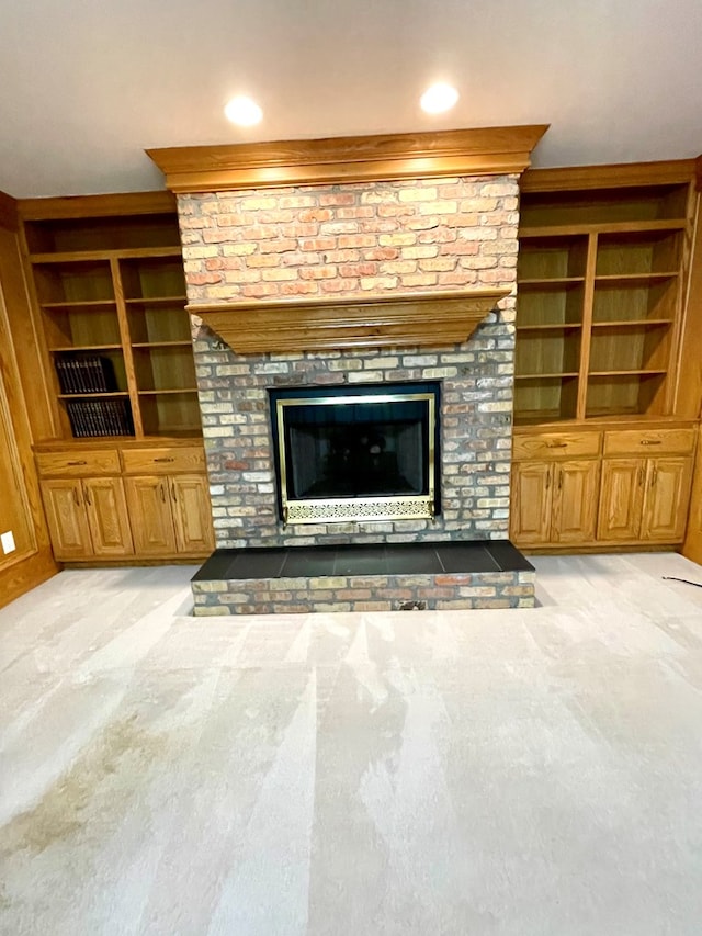 unfurnished living room featuring a brick fireplace, light colored carpet, and built in shelves