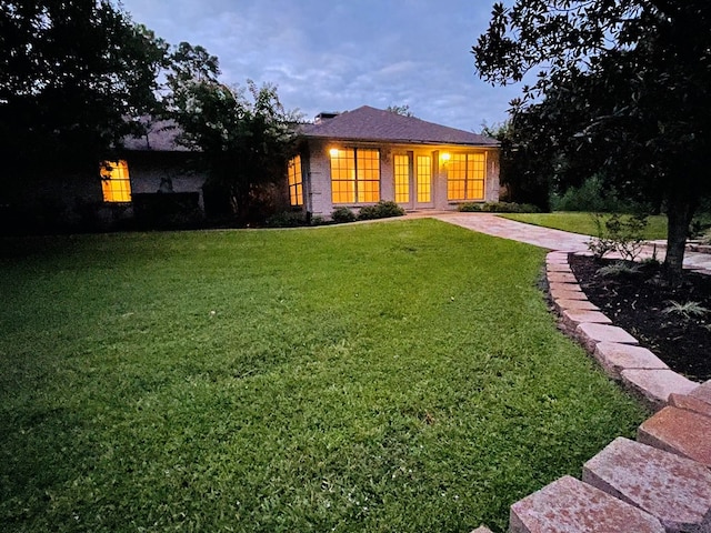 back house at dusk with a lawn and french doors