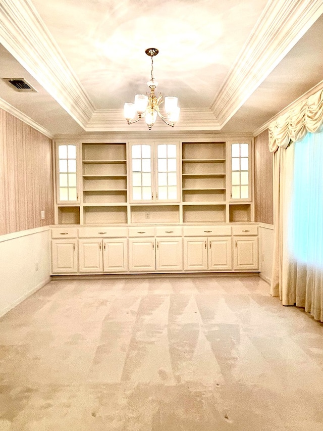 spare room featuring built in shelves, a chandelier, ornamental molding, a raised ceiling, and light colored carpet