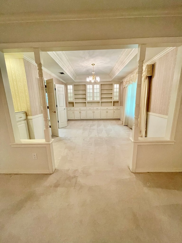 interior space with crown molding, a raised ceiling, an inviting chandelier, and built in shelves