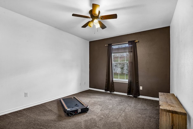 empty room featuring dark colored carpet, a ceiling fan, and baseboards