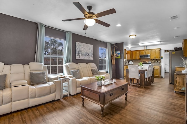 living area featuring plenty of natural light, dark wood finished floors, visible vents, and a ceiling fan