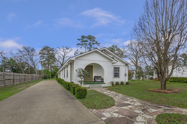 view of front of home with a front yard, brick siding, fence, and driveway