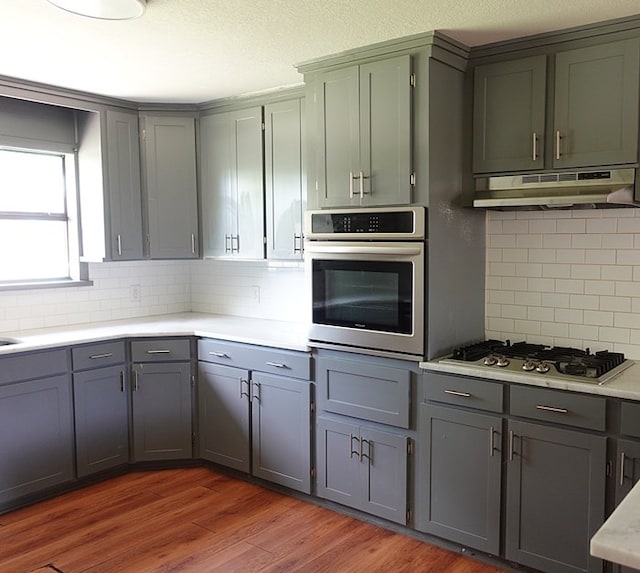 1009 Mockingbird Ln, Nacogdoches, TX 75964 - kitchen featuring appliances with stainless steel finishes, under cabinet range hood, decorative backsplash, gray cabinets, and light countertops