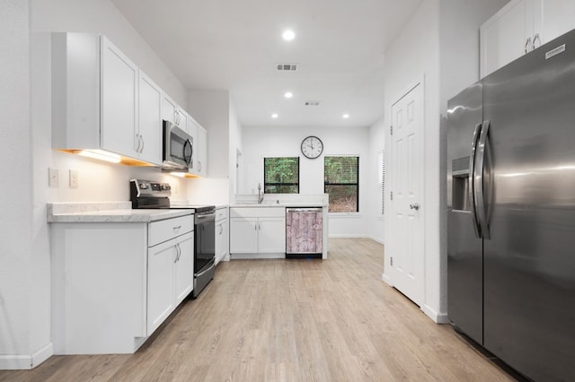 kitchen featuring appliances with stainless steel finishes, a peninsula, light countertops, light wood-style floors, and white cabinetry