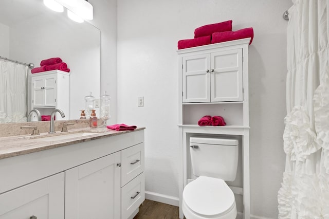 bathroom featuring toilet, baseboards, wood finished floors, and vanity