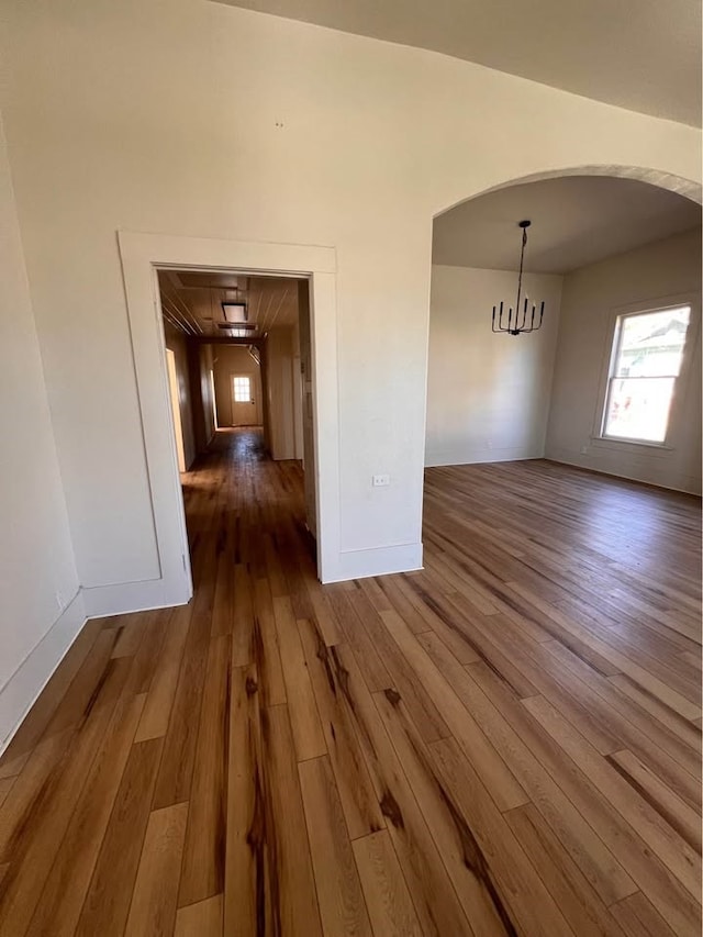 unfurnished dining area with arched walkways, an inviting chandelier, wood finished floors, and baseboards