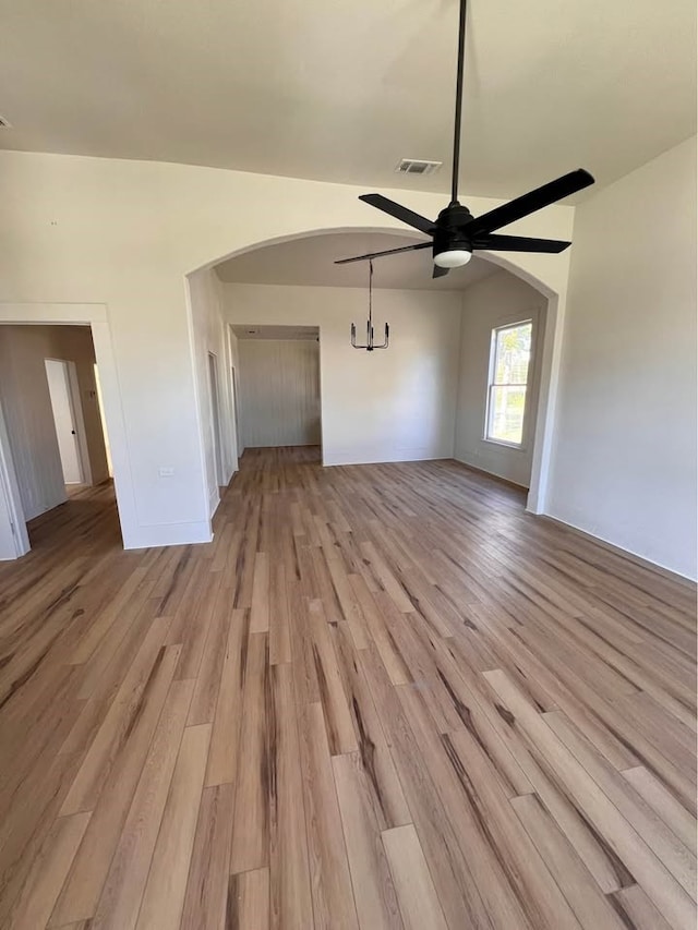 unfurnished living room featuring light wood-type flooring, ceiling fan, visible vents, and arched walkways