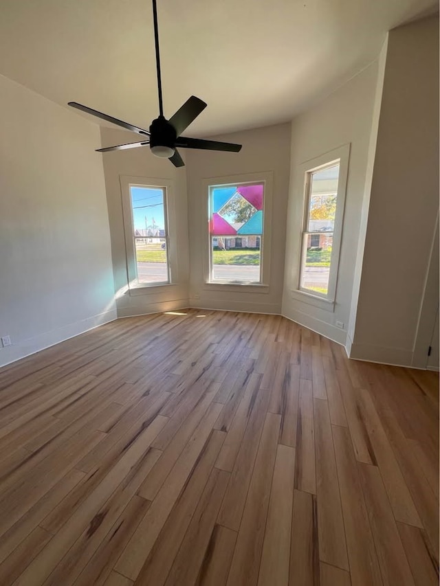 unfurnished room featuring plenty of natural light, wood finished floors, a ceiling fan, and baseboards