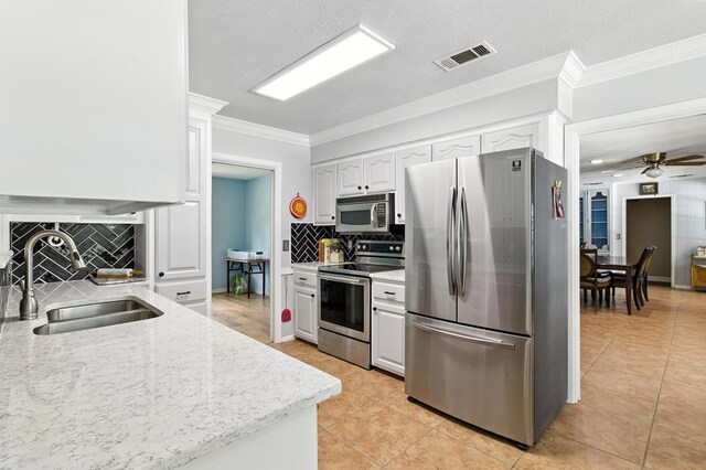 3198 Old Union Rd, Lufkin, TX 75904 - kitchen featuring stainless steel appliances, tasteful backsplash, light tile patterned flooring, white cabinets, and ornamental molding