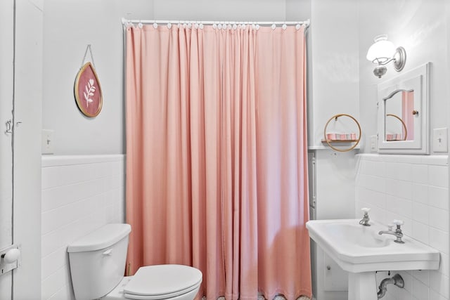 bathroom featuring toilet, tile walls, and sink