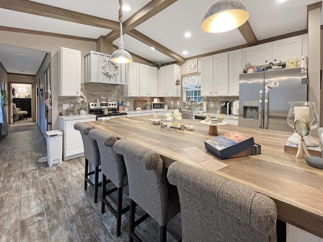 kitchen with hanging light fixtures, stainless steel appliances, lofted ceiling with beams, white cabinets, and decorative backsplash