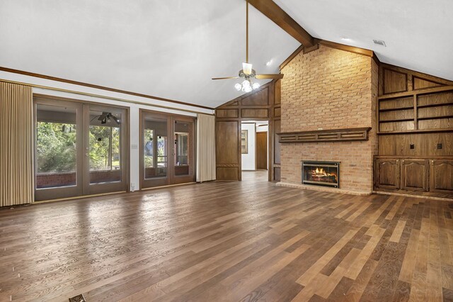 unfurnished living room with ceiling fan, a brick fireplace, lofted ceiling with beams, hardwood / wood-style floors, and wooden walls