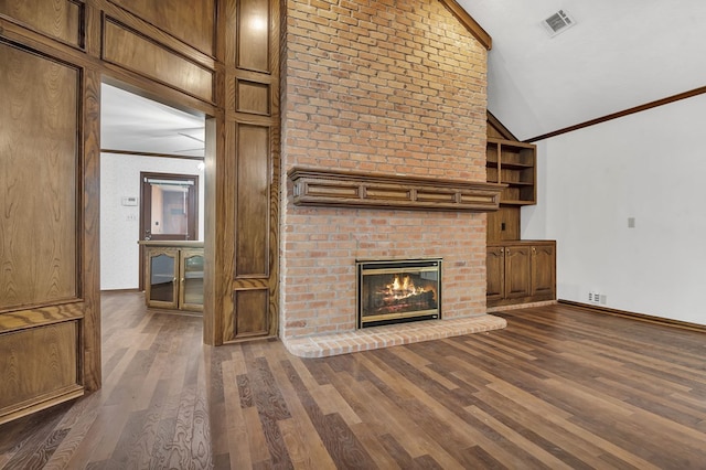 unfurnished living room with dark hardwood / wood-style flooring, built in shelves, vaulted ceiling, crown molding, and a fireplace