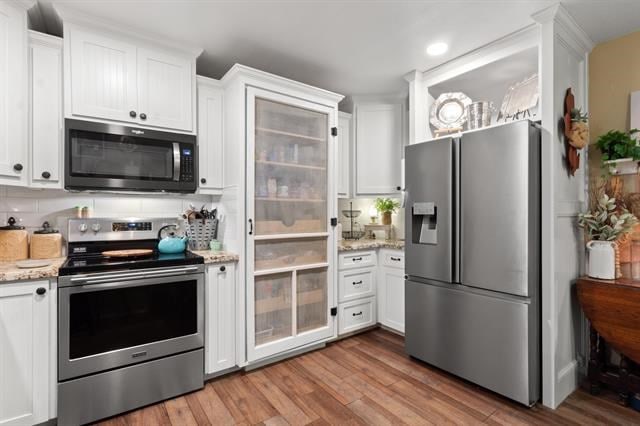 kitchen with light wood-type flooring, stainless steel appliances, light stone countertops, and white cabinetry