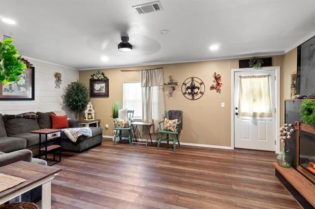 living area with wood finished floors, visible vents, crown molding, baseboards, and ceiling fan