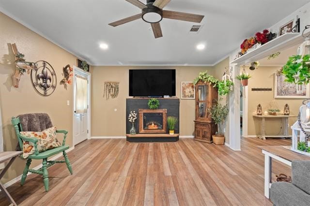 living area featuring ceiling fan, a warm lit fireplace, wood finished floors, and baseboards
