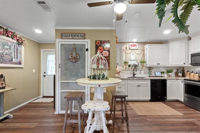 kitchen with a sink, black appliances, ornamental molding, dark wood-type flooring, and visible vents