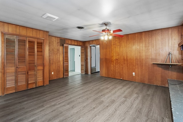 unfurnished living room with hardwood / wood-style floors, ceiling fan, and wood walls