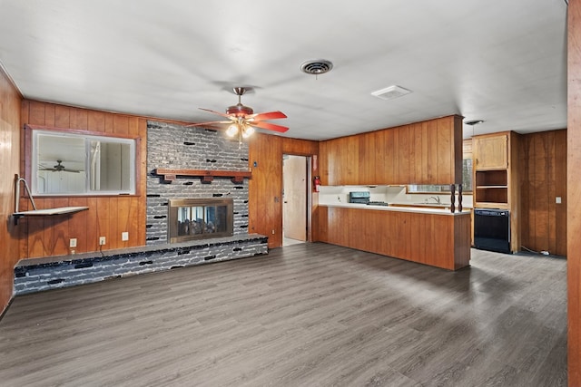 kitchen featuring kitchen peninsula, dark hardwood / wood-style flooring, a brick fireplace, black dishwasher, and wood walls