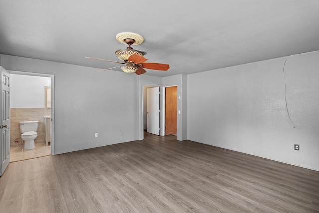 interior space featuring light wood-type flooring, connected bathroom, ceiling fan, and tile walls