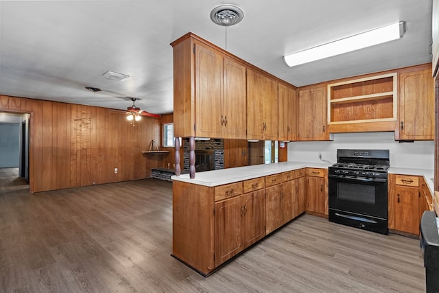 kitchen featuring kitchen peninsula, ceiling fan, wooden walls, light hardwood / wood-style flooring, and black gas range