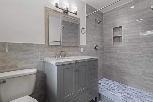 bathroom featuring tiled shower, vanity, toilet, and tile walls