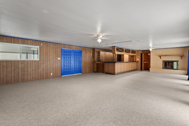 unfurnished living room with carpet flooring, a textured ceiling, ceiling fan, and wooden walls