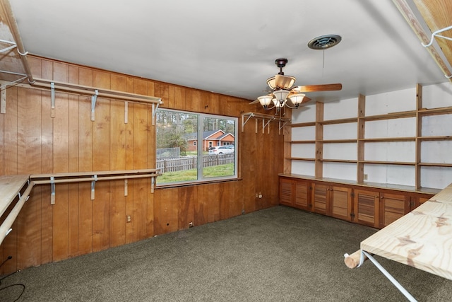 interior space with wooden walls, carpet floors, and ceiling fan