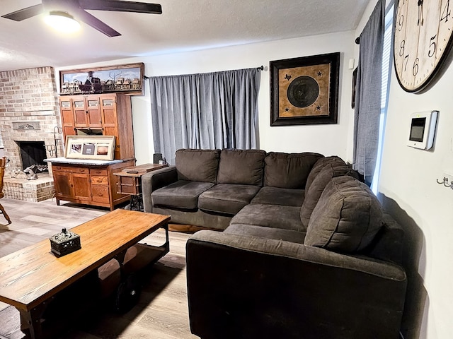 living room with a textured ceiling, light wood-type flooring, and a brick fireplace