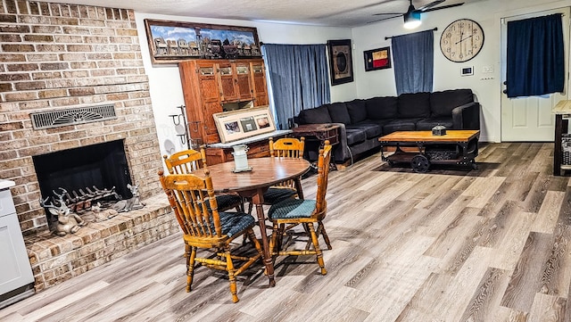 dining space with hardwood / wood-style flooring, ceiling fan, a fireplace, and a textured ceiling