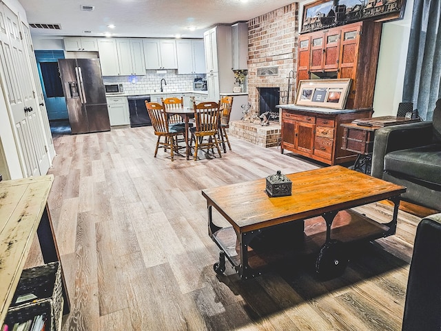 living room with sink, light hardwood / wood-style flooring, a textured ceiling, and a brick fireplace