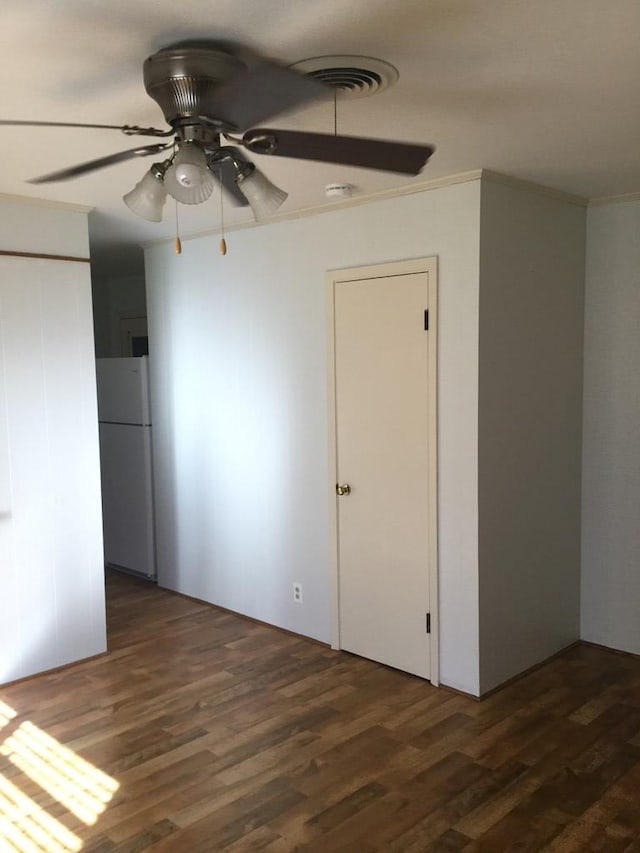 unfurnished bedroom featuring dark hardwood / wood-style flooring, ornamental molding, ceiling fan, and white refrigerator