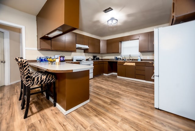 kitchen featuring kitchen peninsula, light wood-type flooring, white appliances, sink, and a breakfast bar area