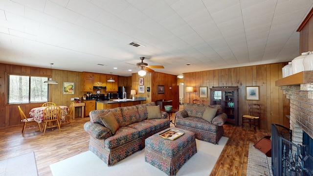 living area with visible vents, light wood-style flooring, ceiling fan, and a brick fireplace